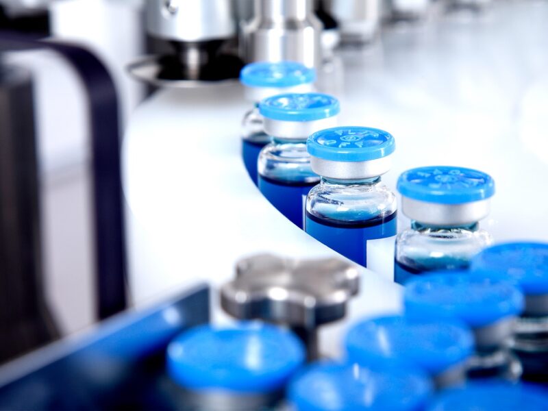 Garrafas de vidro em produção na bandeja de um distribuidor líquido automático, uma linha para encher medicamentos contra bactérias e vírus, antibióticos e vacina